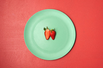 One strawberry cut in half on green plate. Two strawberry halves