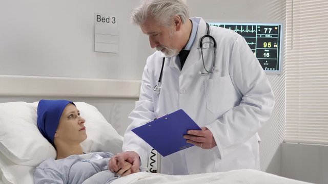 doctor talking with a patient suffering from cancer lying in a hospital bed showing her medical records results after the surgery