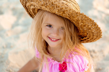 portrait of a little blonde girl in a straw hat in summer on a sandy beach, space for text