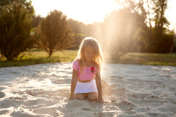 little blonde girl in a straw hat playing with sand on the beach