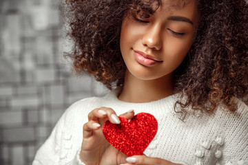 close-up portrait of a young curly-haired African American girl in a white sweater holding a paper...