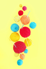 Multi-colored balls of wool yarn of different sizes levitating on a yellow background..