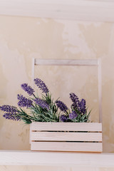 Bunch of lavender and greenery in wooden box vase on a white table on a vintage shelf over pastel wall. Chic provence interior decor for farm home style. Provence home decoration.