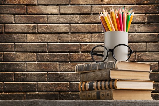 Stack of vintage books, glasses and colorful pencils on the desk