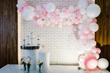 Poster Photo-wall, wedding decoration space or place from white and pink balloons and white brick wall near table with a wedding cake, candles and flowers. © Serhii