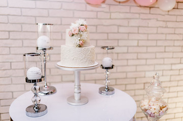 Table with a wedding cake, candles and flowers. Photo-wall, wedding decoration space or place from white and pink balloons and white brick wall.