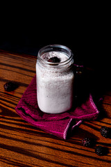 Smoothie de frambuesa con frambuesa regadas en trapo guinda en fondo negro sobre madera