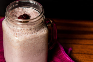 Smoothie de frambuesa con frambuesa regadas en trapo guinda en fondo negro sobre madera