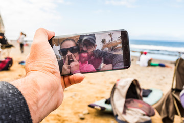 Man point of view of funny crazy couple having fun taking selfie or doing video conference call from the beach using a modern technology connected smart phone