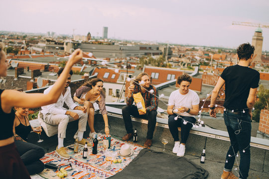 Friends looking at man and woman playing with string light while enjoying in rooftop party