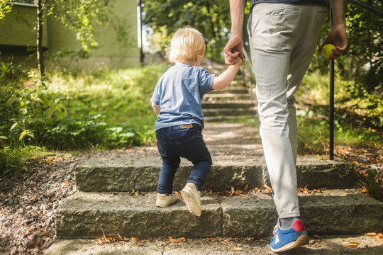 Low section of man and son holding hands while moving up on steps at park