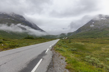 The road leading a mysterious gorge surrounded by clouds of the Norwegian mountains, selective focus