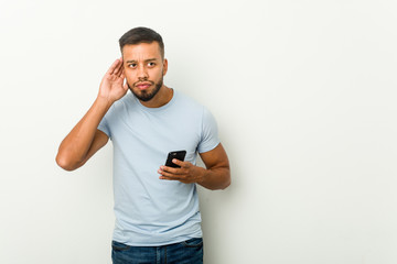 Young mixed race asian man holding a phone trying to listening a gossip.