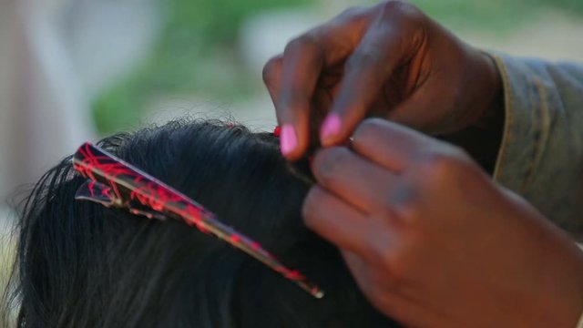 A dark-skinned girl braids pigtails with red threads to a girl