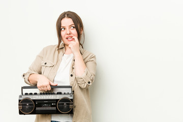 Young curvy woman holding a retro radio relaxed thinking about something looking at a copy space.