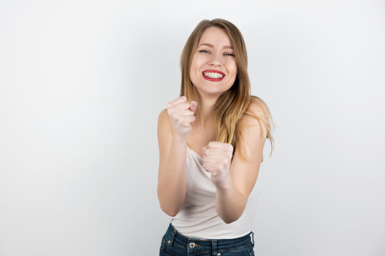 young beautiful blond woman standing on isolated white background in boxing position looking excited and happy, splash of emotions
