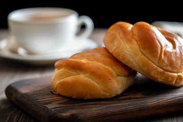 Fresh and rosy buns with cherry on a wooden table and a cup with fragrant tea.