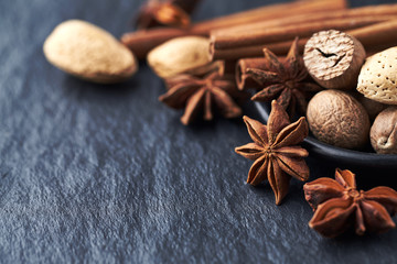 Star anise, nutmeg and cinnamon sticks on black stone background. Copy space. 