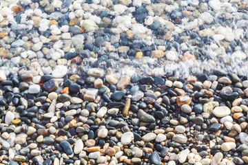 Sea coast covered with colorful pebbles. Soft transparent wave, marine background.