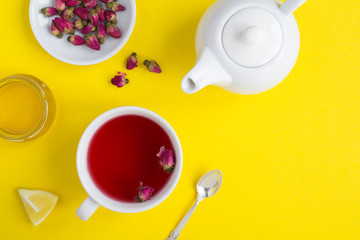 Herbal tea with pink roses in the white cup  on the yellow  background. Top view. Copy space.
