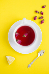 Herbal tea with pink roses in the white cup  on the yellow  background. Top view. Location vertical. Copy space.