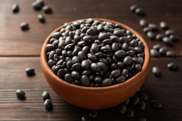 Black beans in ceramic bowl on dark wooden background. Selective focus.