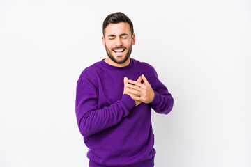 Young caucasian man against a white background isolated laughing keeping hands on heart, concept of happiness.