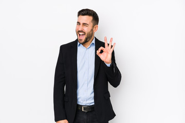 Young caucasian business man against a white background isolated winks an eye and holds an okay...