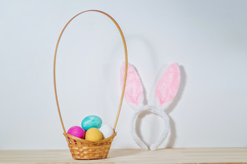 colored Easter eggs in a wooden basket on the table. rabbit ears on the background. Easter bunny