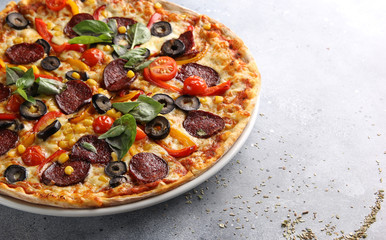 The concept of Italian cuisine. Pepperoni pizza with tomatoes, basil, corn and olives on a light background. Background image, copy space