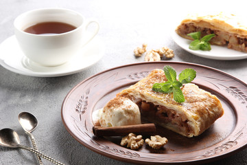 Concept of German cuisine. Apple strudel with cinnamon, nuts and ice cream with a cup of tea on a light background. Background image, copy space