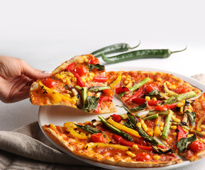 The concept of Italian cuisine. Vegetable pizza with tomatoes, peppers, corn and asparagus on a light background with hand. Background image, copy space