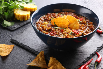 Concept of Mexican cuisine. Thick  soup with meat, corn and chili peppers on a black background. Nachos with cilantro near bowl. Background image, copy space