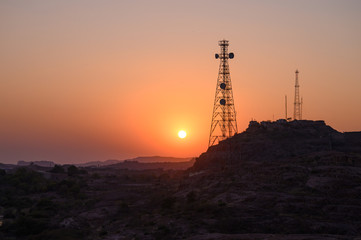 Telecommunication towers on hill in remote control area aganist sunset sky