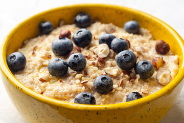 Oatmeal porridge with hazelnuts and blueberries in bowl on concrete background. Selective focus.
