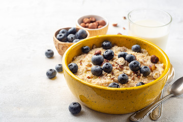 Oatmeal porridge with hazelnuts and blueberries in bowl on concrete background. Selective focus.