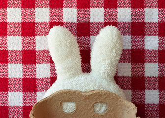 White toweling bunny ears with a carboard mask. Red square tablecloth in the background.