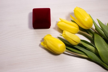 Flower tulip on white wooden background. Bouquet of the yellow tulip flowers. Valentines day concept, woman's day. Red gift box.  Letter or invitation in a silver envelope.