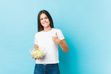 Young caucasian woman holding a salad smiling and raising thumb up