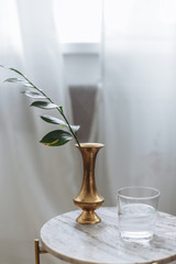 Gold vase with garnish with greens  marble backsplash wooden board white drapes glass water in cozy scandinavian interior © Andrey