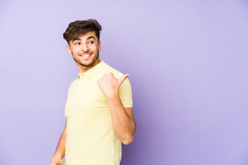 Young arabian man isolated on a purple background points with thumb finger away, laughing and carefree.