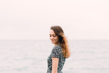 a young girl in a dress from the back stands on the beach on large stones