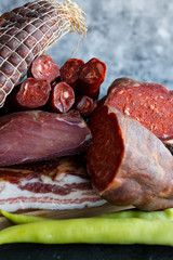 Different types of sausages and smoked meats on dark background.
