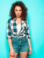 Portrait of beautiful smiling model with afro curls hairstyle dressed in summer hipster clothes.Sexy carefree girl posing in studio near blue wall.Trendy funny and positive woman © halayalex