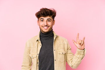 Young arabian man posing in a background isolated showing a horns gesture as a revolution concept.