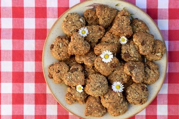 Homemade whole grain round and heart shaped cookies with several kinds of seeds, raisins, ground nuts, oatmeal. Romantic concept, decorated with daisies