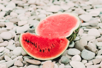 two halves of cut ripe watermelon on the beach with pebbles