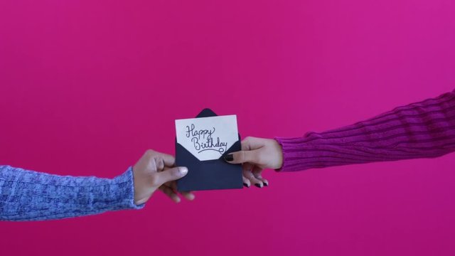 Women hands and arms exchanging happy birthday card with saturated pink backgrou