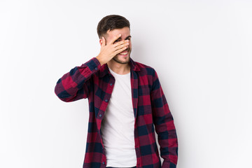 Young caucasian man posing in a white background isolated blink at the camera through fingers, embarrassed covering face.