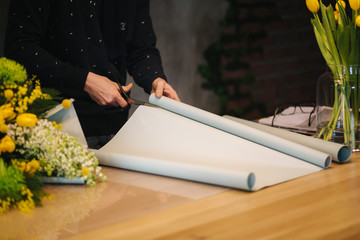 Male make spring bouquet. Man florist wrapping beautiful bouquet of spring flowers in pack paper on the wooden table. Beautiful flower composition of yellow flowers